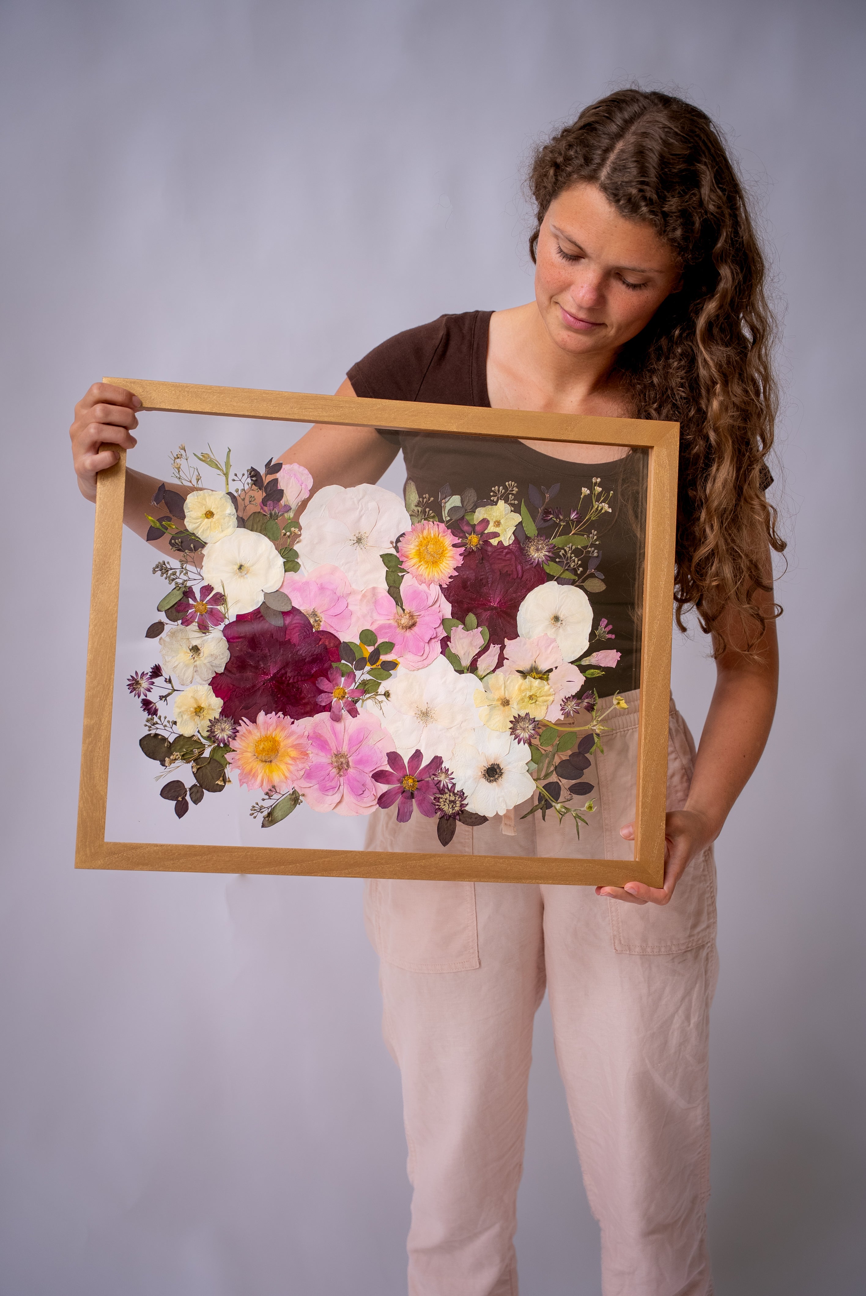Woman holding a framed floral arrangement against a gray background